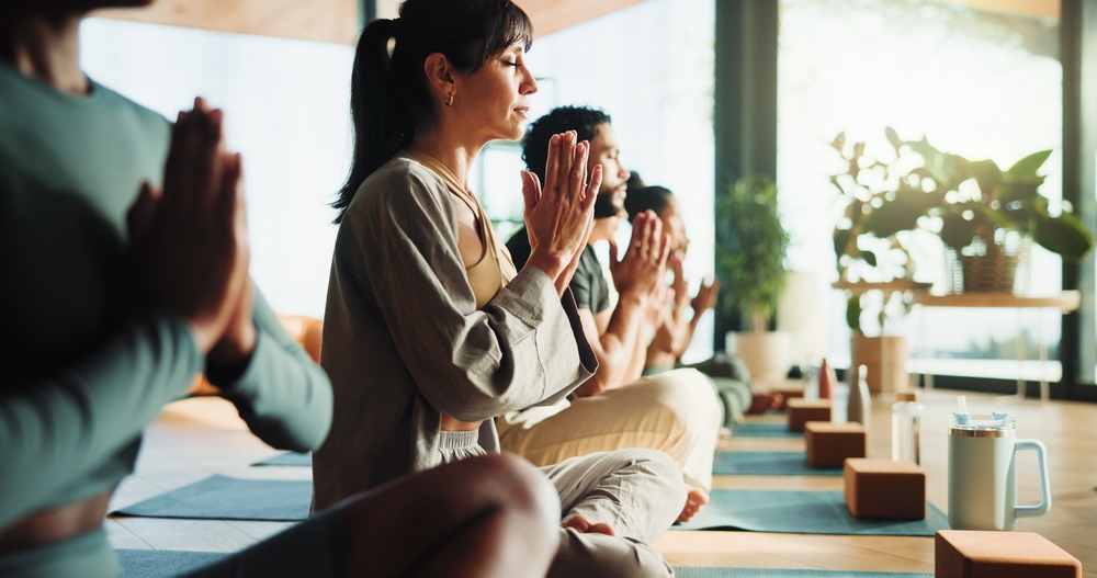 Personnes se relaxant dans une ambiance zen pendant un cours de yoga, les mains jointes en position de prière