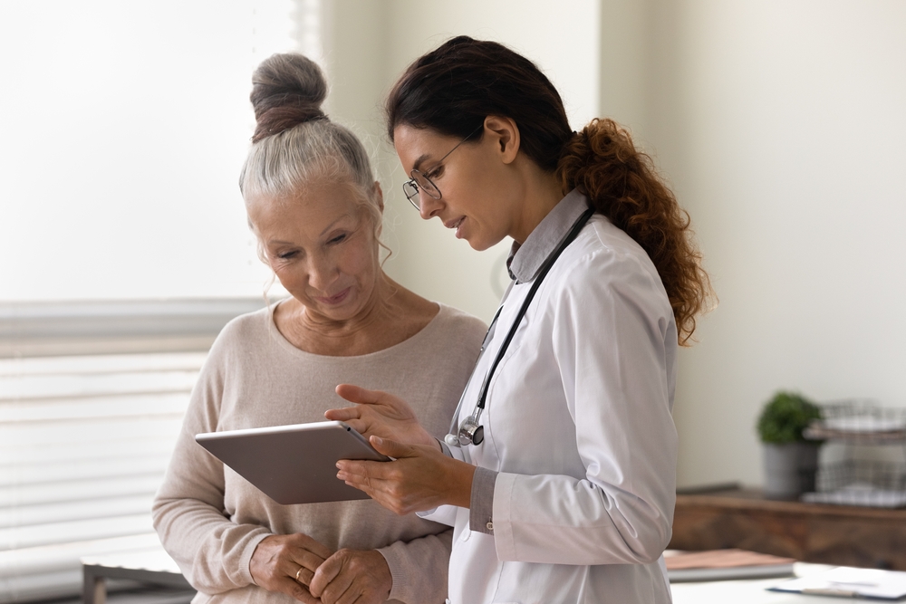 Médecin généraliste sérieux montrant l'écran d'une tablette à une femme d'environ 70 ans